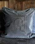 Gray pillow with unicorn embroidery on a bed with wooden headboard