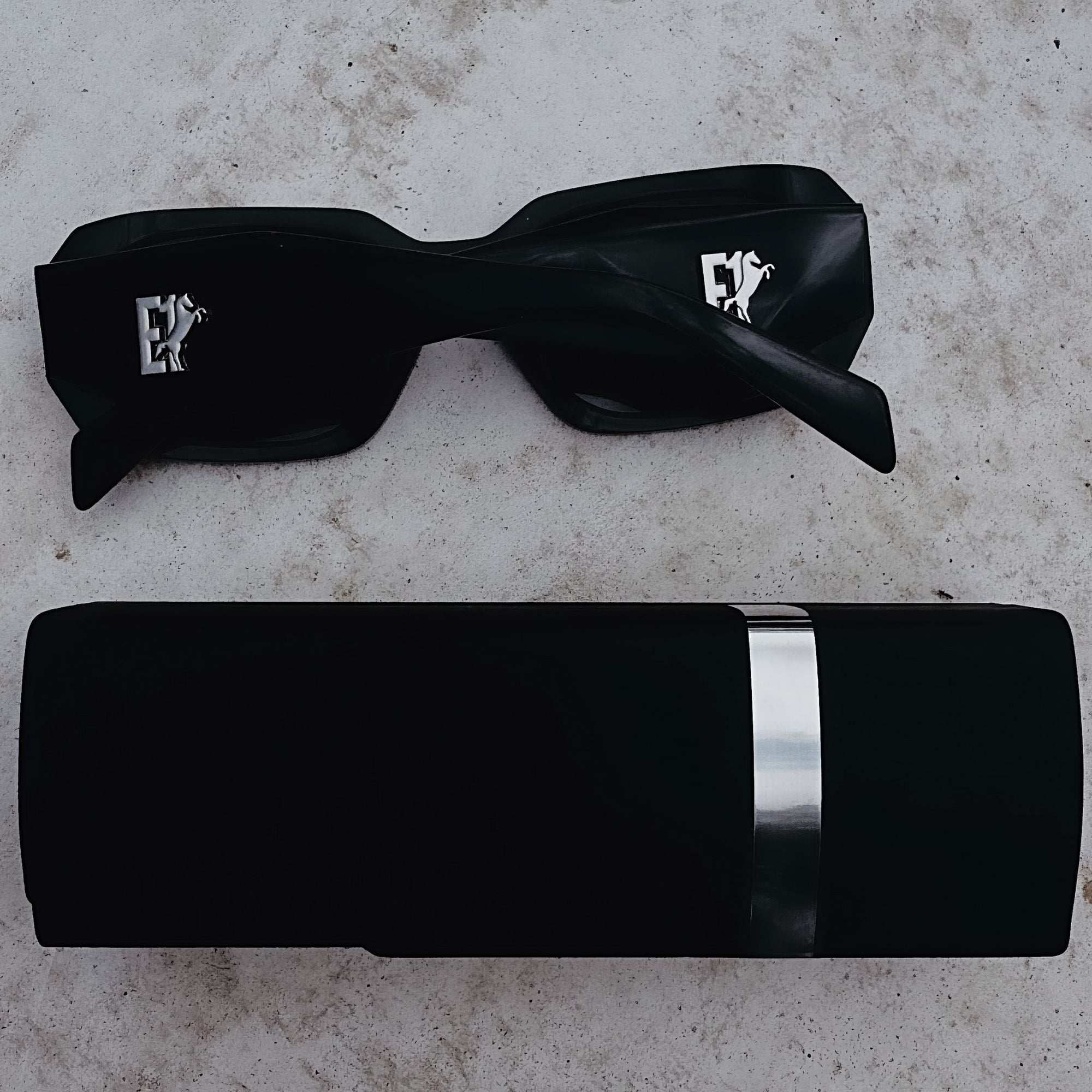 Black sunglasses from E1 Equestrian with a reflective lens on a textured surface